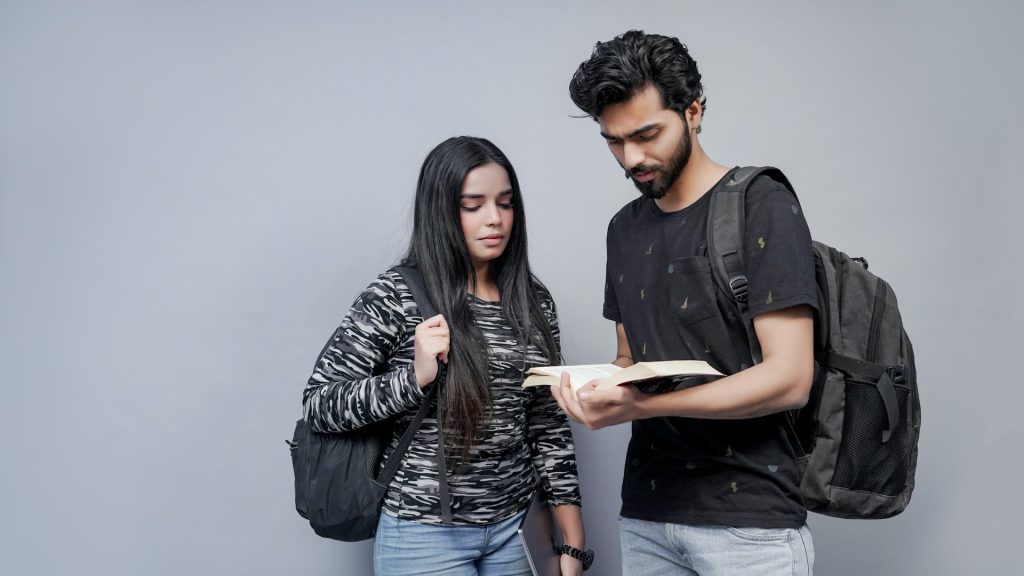male and female student are standing and reading a textbook
