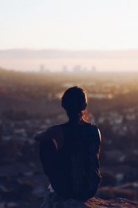 A person stands at the top of a hill looking over a town or city.