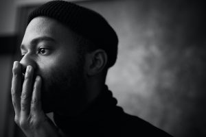 A black and white photo of a man thinking with his hand over his mouth.