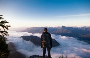 man in black jacket and black pants standing on rock formation looking at the mountains