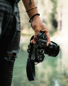 Tattooed arm with bracelets holding a camera