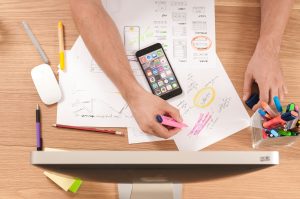 two hands highlighting information on a sheet of paper. There is a iphone resting in the desk