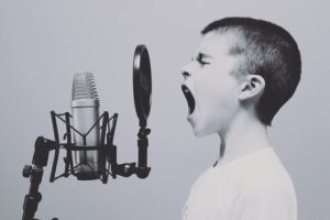 A young boy yells into an old fashioned mic